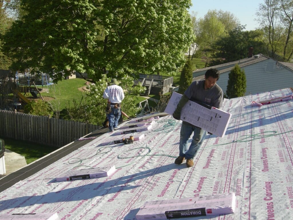 A man carrying bundles of shingles on top of a new roof.