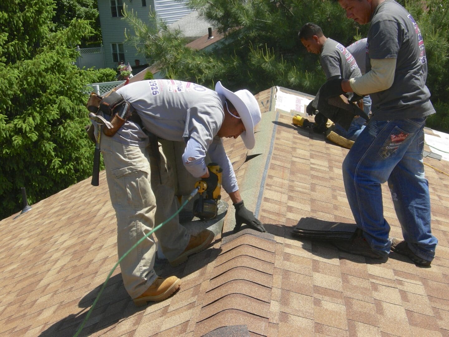 men installing roof shingles on the ridge of a house.