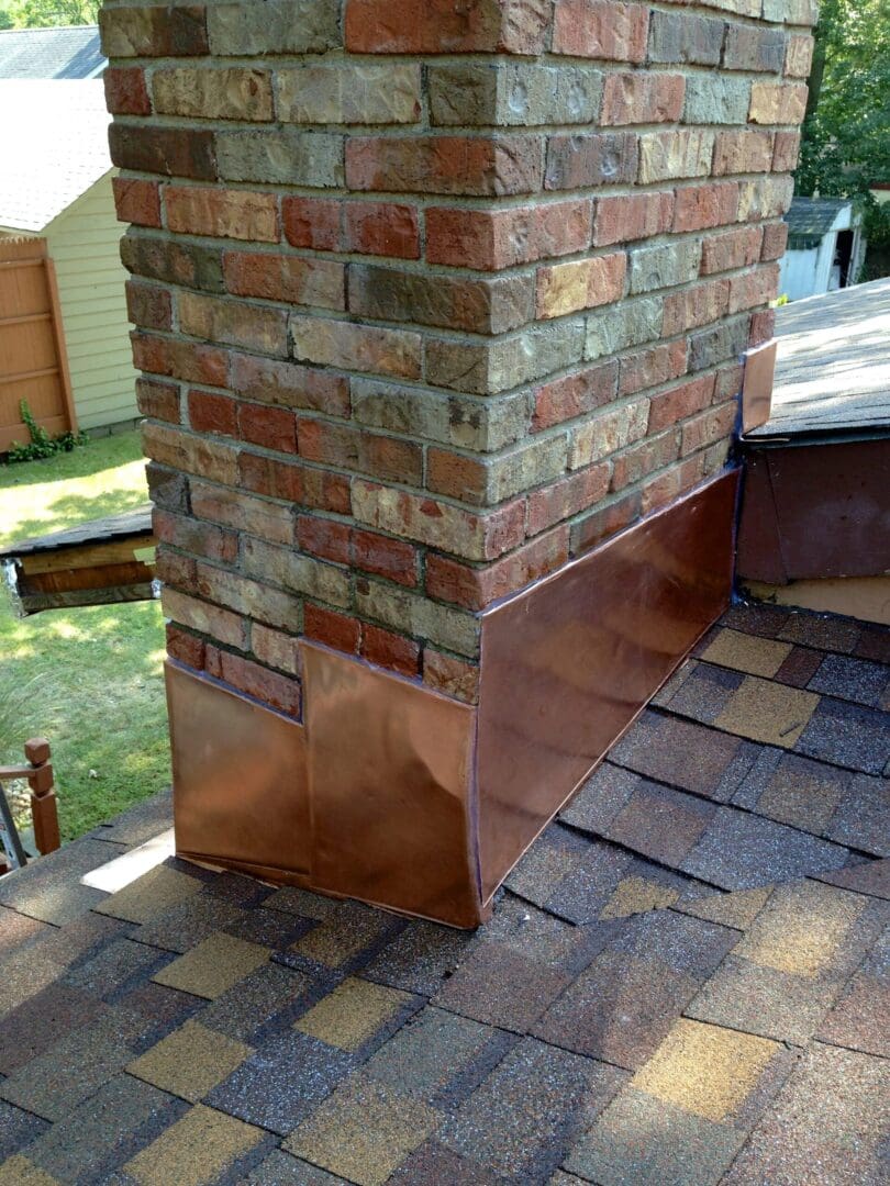 A brick chimney with copper flashing on the roof.