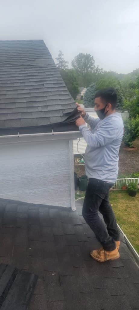 A man standing on top of a roof checking roof shingles. Arrange for a nj roofing inspection.