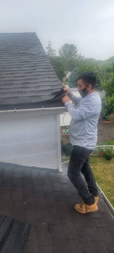 A man standing on top of a roof checking roof shingles