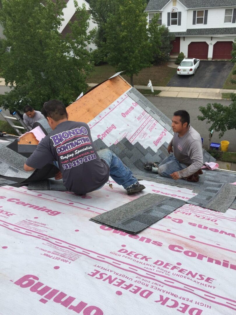 Two men applying shingles on the roof of a house