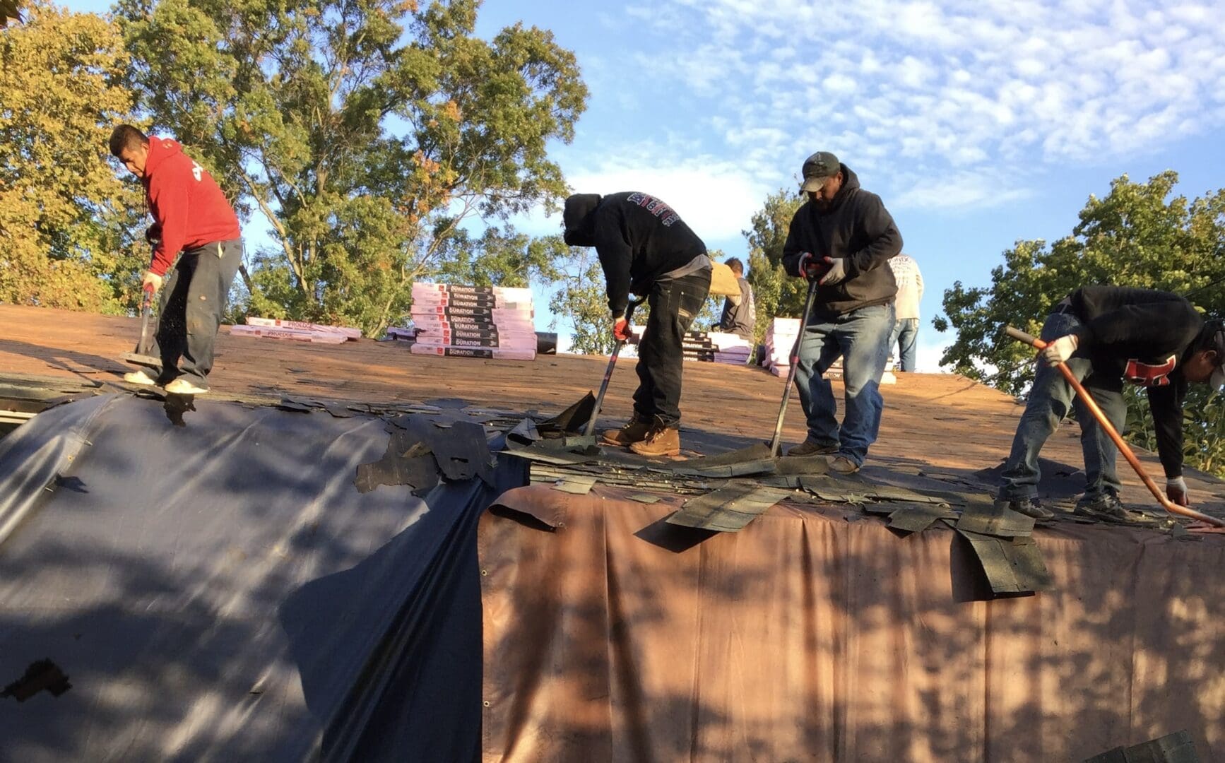 Two men working on a tarp covering a roof.