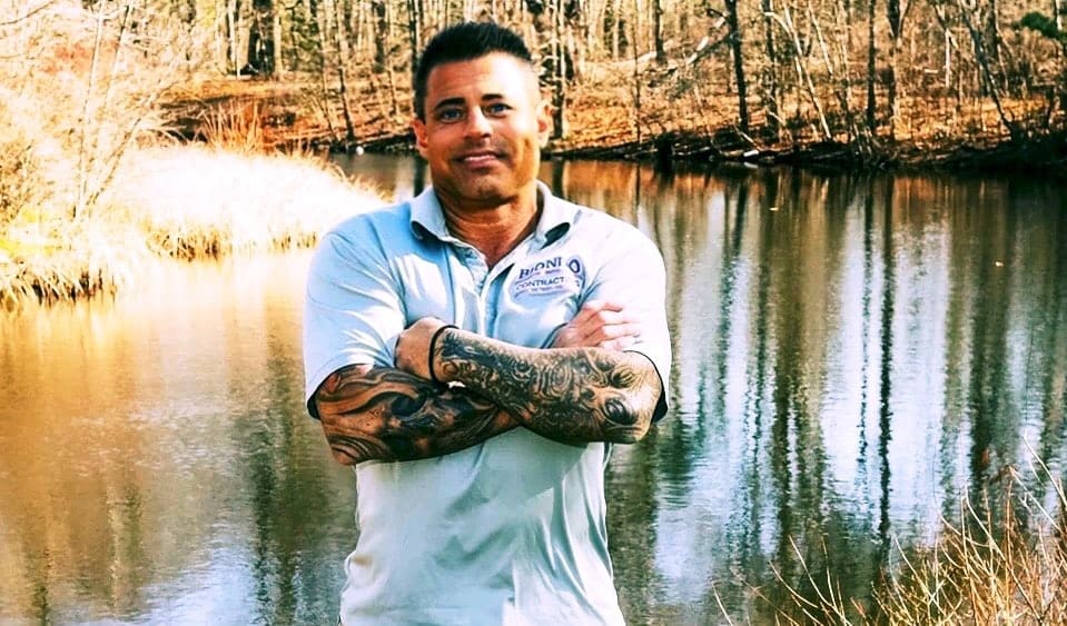 A man with tattoos standing in front of water.