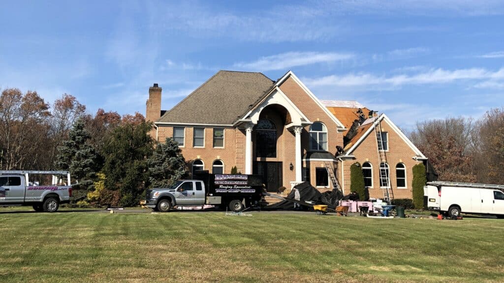 A roofing truck parked in front of a large house, new roof installation