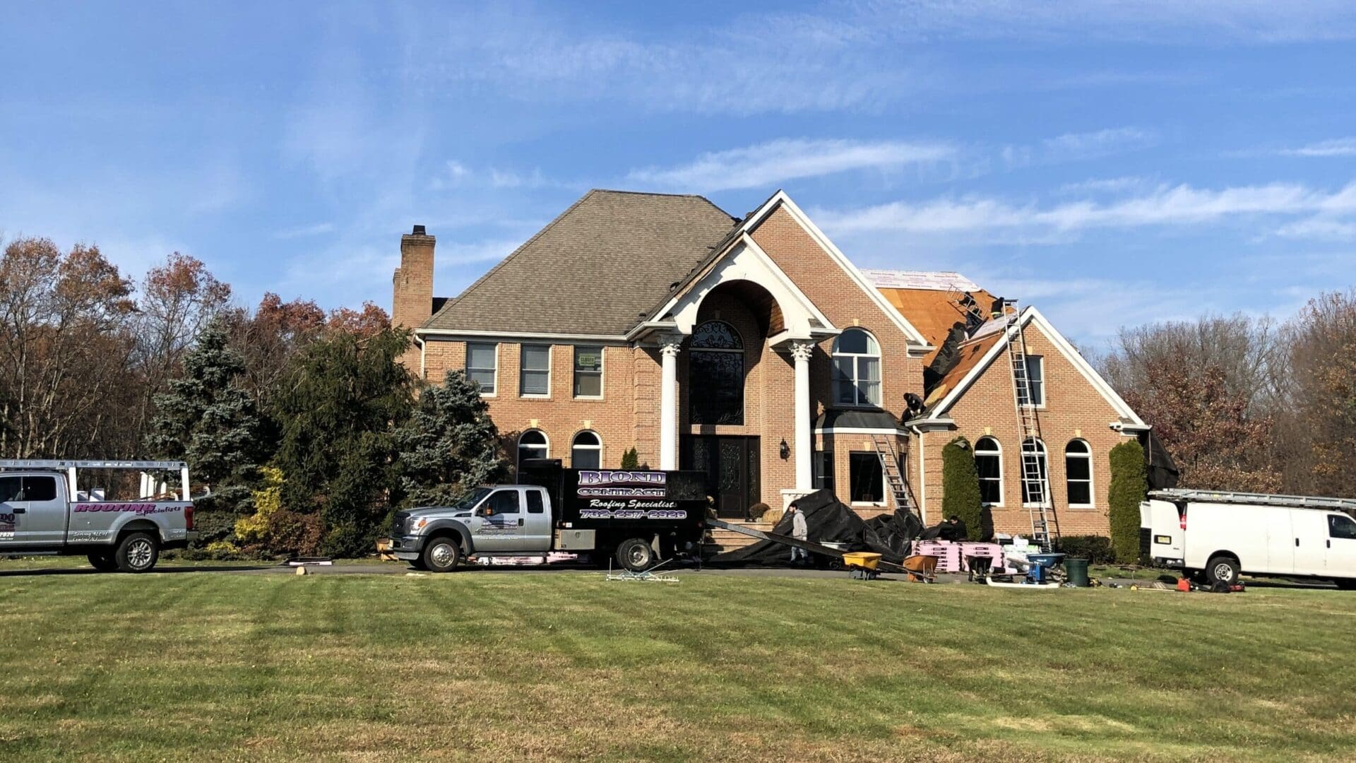 A roofing truck parked in front of a large house.