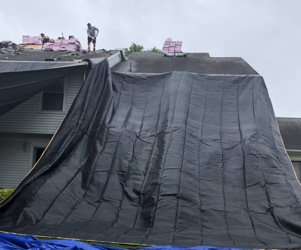 Tarped draped from from roof to ground, performing a professional roofing company work ethic.